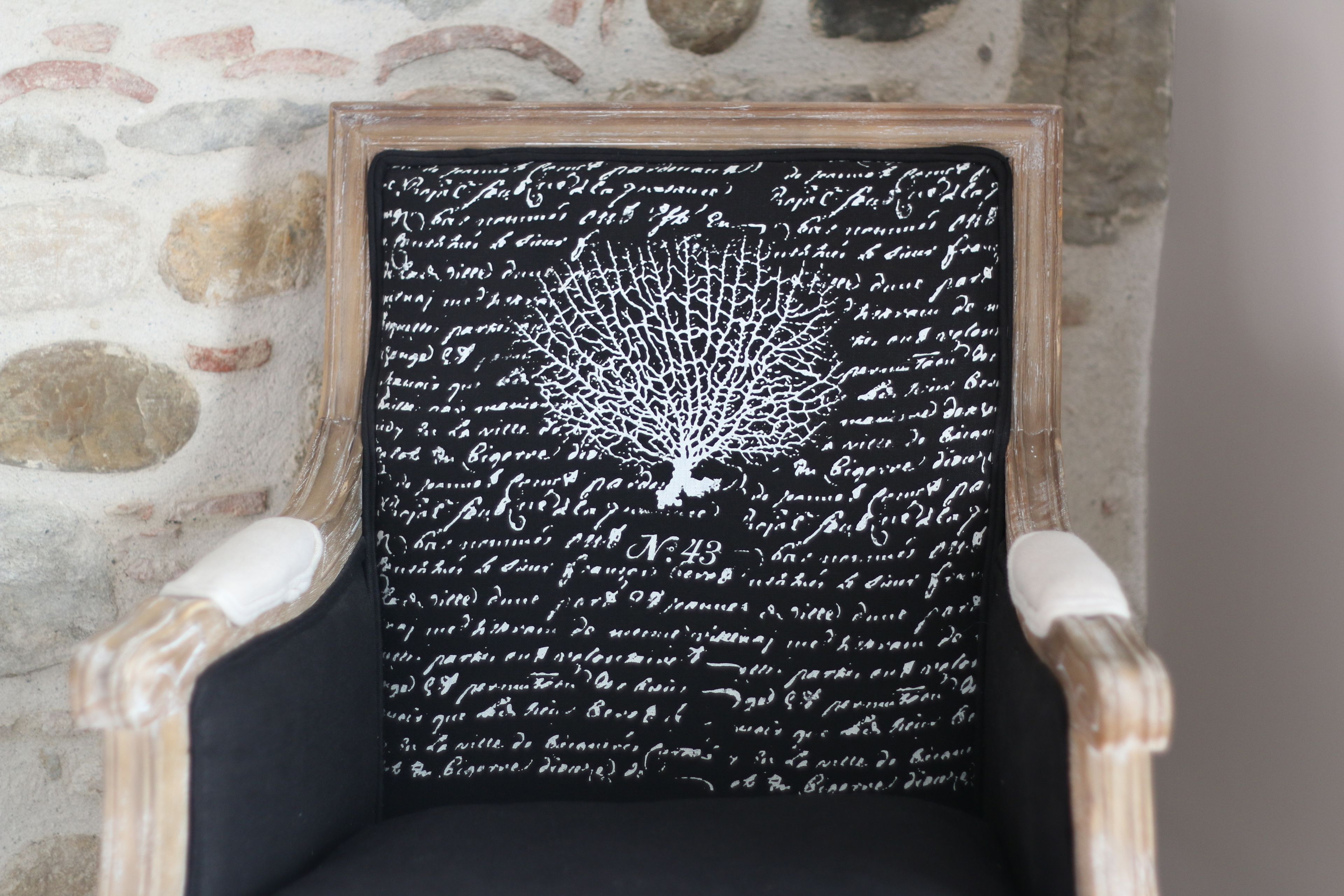 Una silla con asiento negro y letras blancas, frente a un muro de piedra.