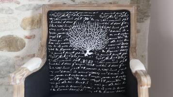 Una silla con asiento negro y letras blancas, frente a un muro de piedra.