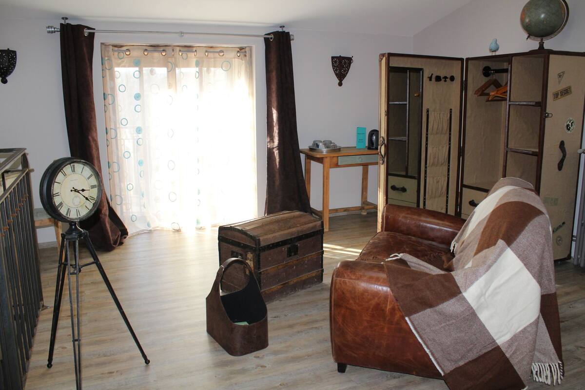 Una sala de estar con un sofá de cuero marrón, una mesa de centro de madera, un reloj, un baúl y un armario.