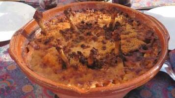 Una olla de barro grande llena de un plato al horno, posiblemente una cazuela, sobre una mesa con mantel estampado.