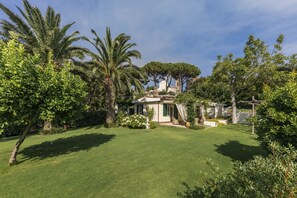 A well-maintained garden with a variety of trees and shrubs, a clear pathway leading to a building with a white facade and a dome structure. - La residEnza 2-Villa in Ravello in a central position with parking and garden. (Ravello)