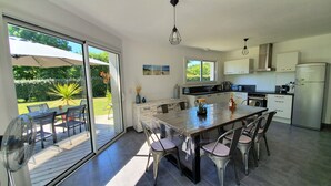 A modern kitchen with a large island, sliding glass doors to a patio, and a view of a garden. - Beautiful new villa, quiet, near forest Biscarrosse / 6p (Biscarrosse)