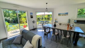 A modern kitchen with a dining area, large sliding glass doors leading to a garden, and a cozy seating area with a sofa and chairs. - Beautiful new villa, quiet, near forest Biscarrosse / 6p (Biscarrosse)