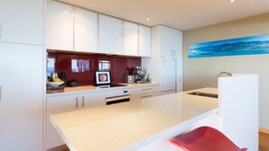 Una cucina moderna con mobili bianchi, un'isola centrale e una sedia rossa.