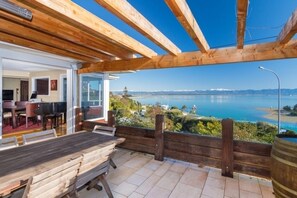 Una terraza de madera con una mesa y sillas, con vista a un cuerpo de agua y montañas distantes.