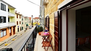 Eine enge Straße mit Häusern an beiden Seiten, einem Balkon mit Tisch und Stühlen und einem sichtbaren Geschäftseingang.
