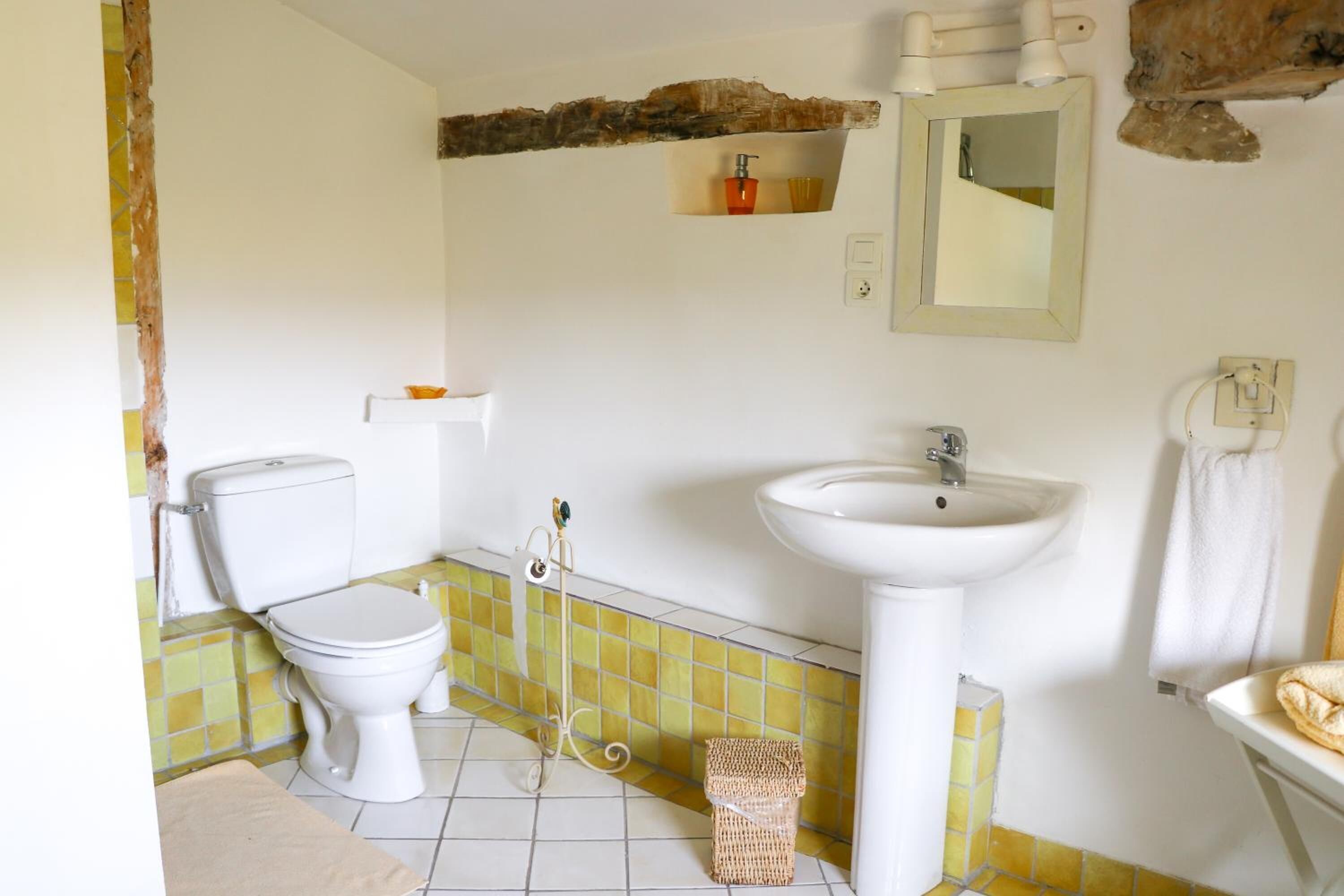 A bathroom with a toilet, sink, and mirror. There is a towel rack and a basket on the floor.