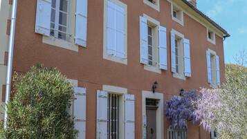 Una casa de dos pisos con contraventanas blancas, un banco y una planta en maceta en el jardín delantero.