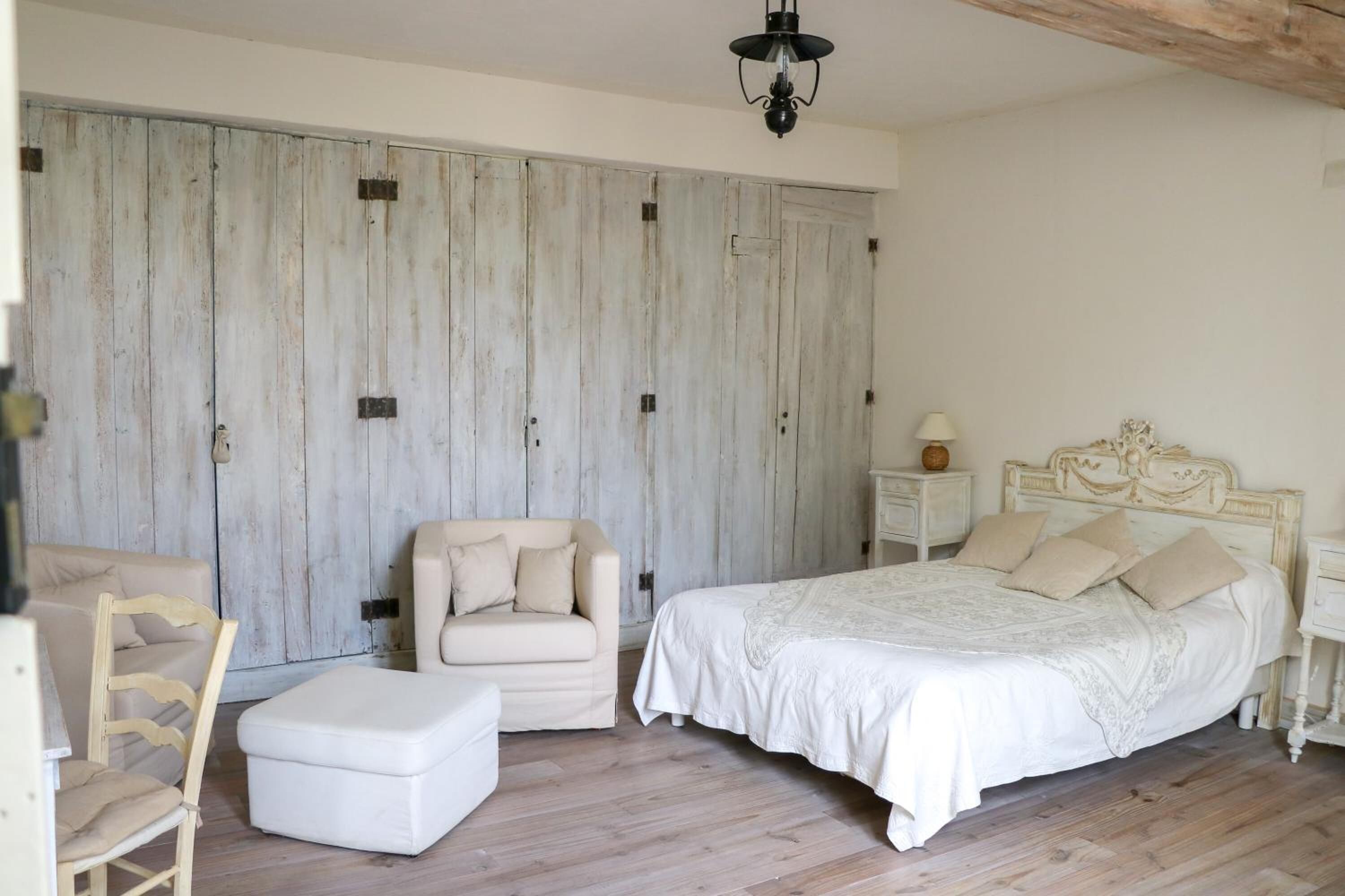 Ein Schlafzimmer mit einem großen Bett, einem Sessel, einem kleinen Hocker, einem Nachttisch und einem Kleiderschrank.