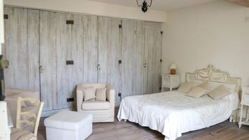 Ein Schlafzimmer mit einem großen Bett, einem Sessel, einem kleinen Hocker, einem Nachttisch und einem Kleiderschrank.