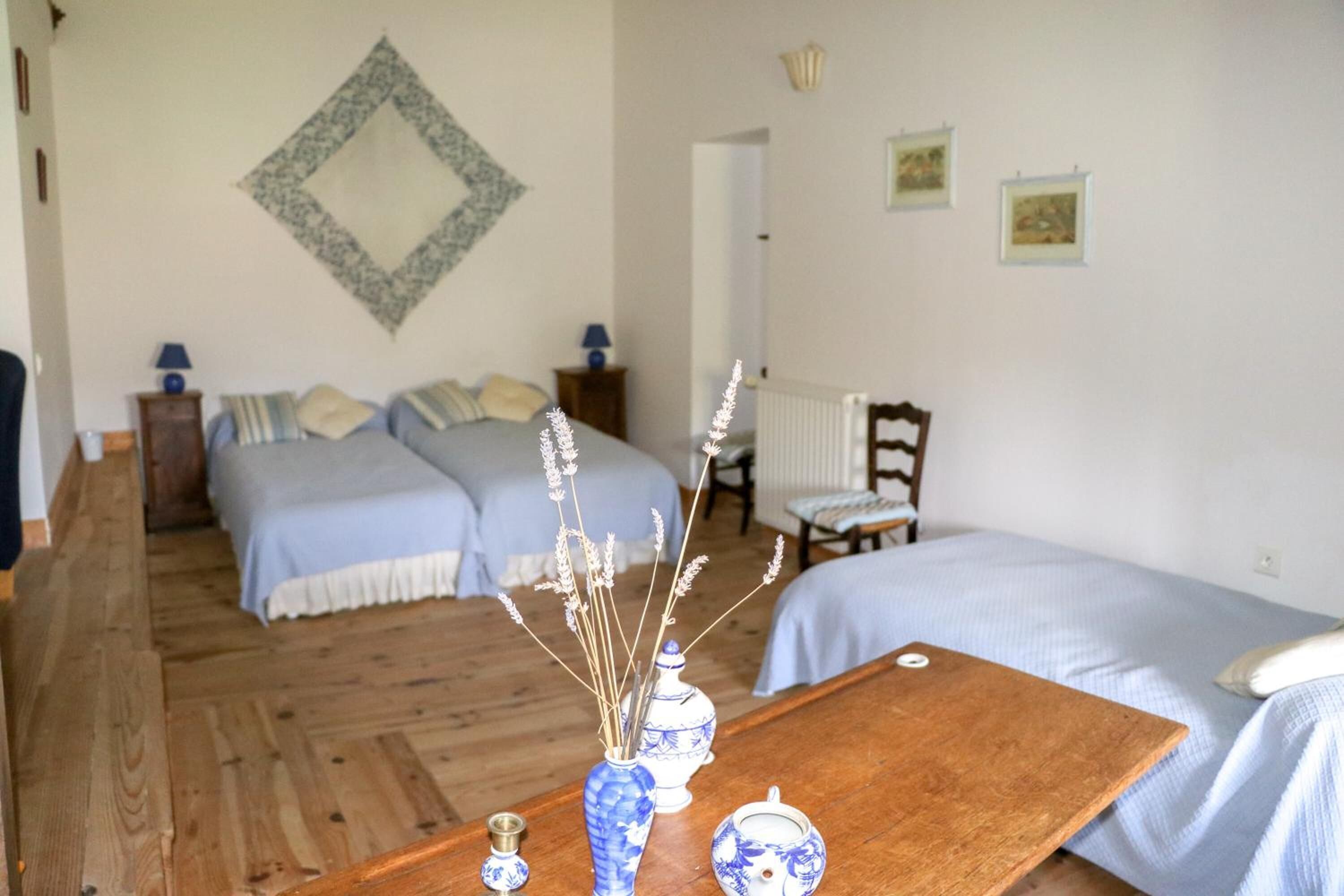 Une chambre avec deux lits, une table en bois agrémentée d’objets décoratifs, un miroir au mur et une petite chaise.