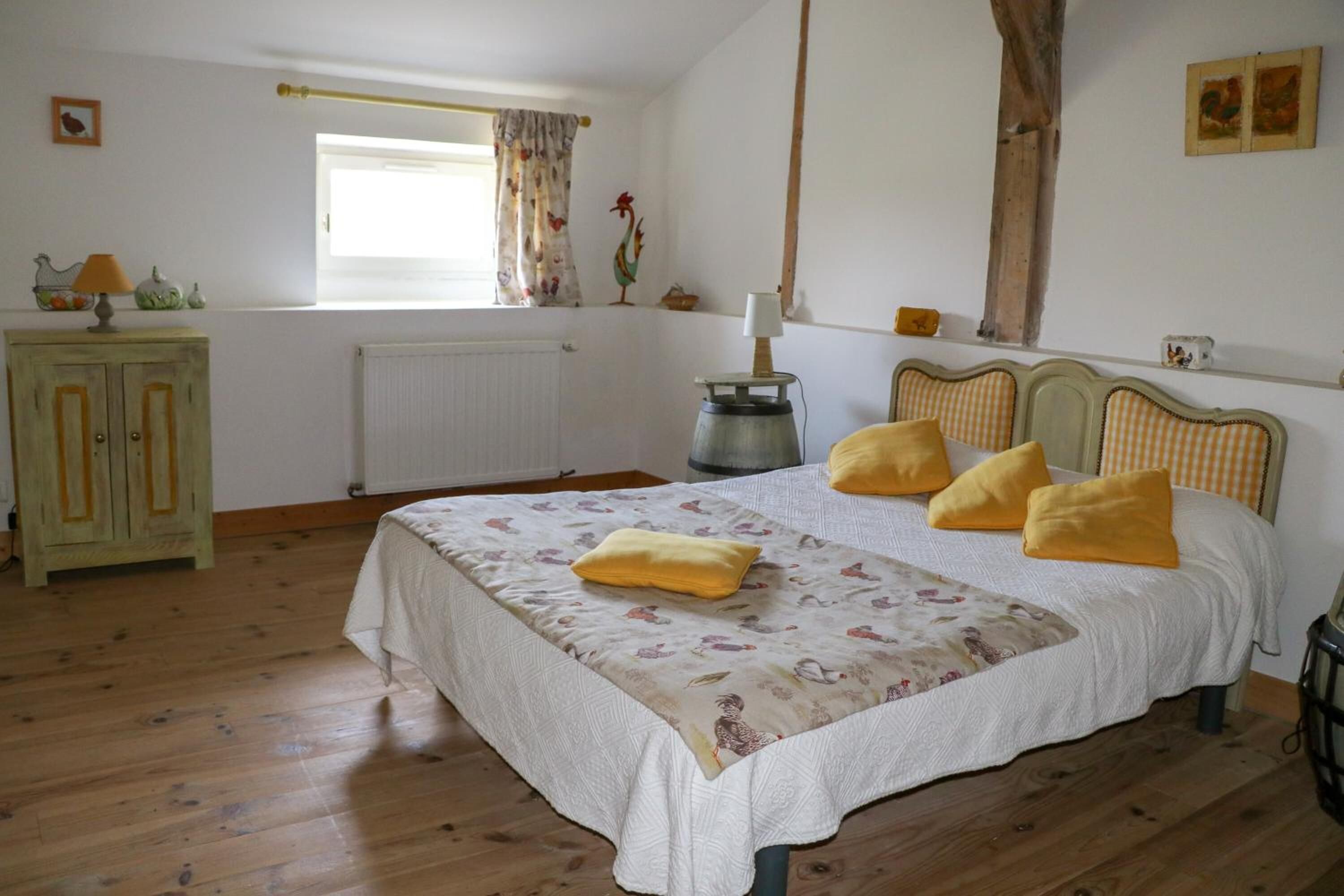 Een slaapkamer met een groot bed, een radiator, een raam met gordijnen, een houten kast en een lamp.