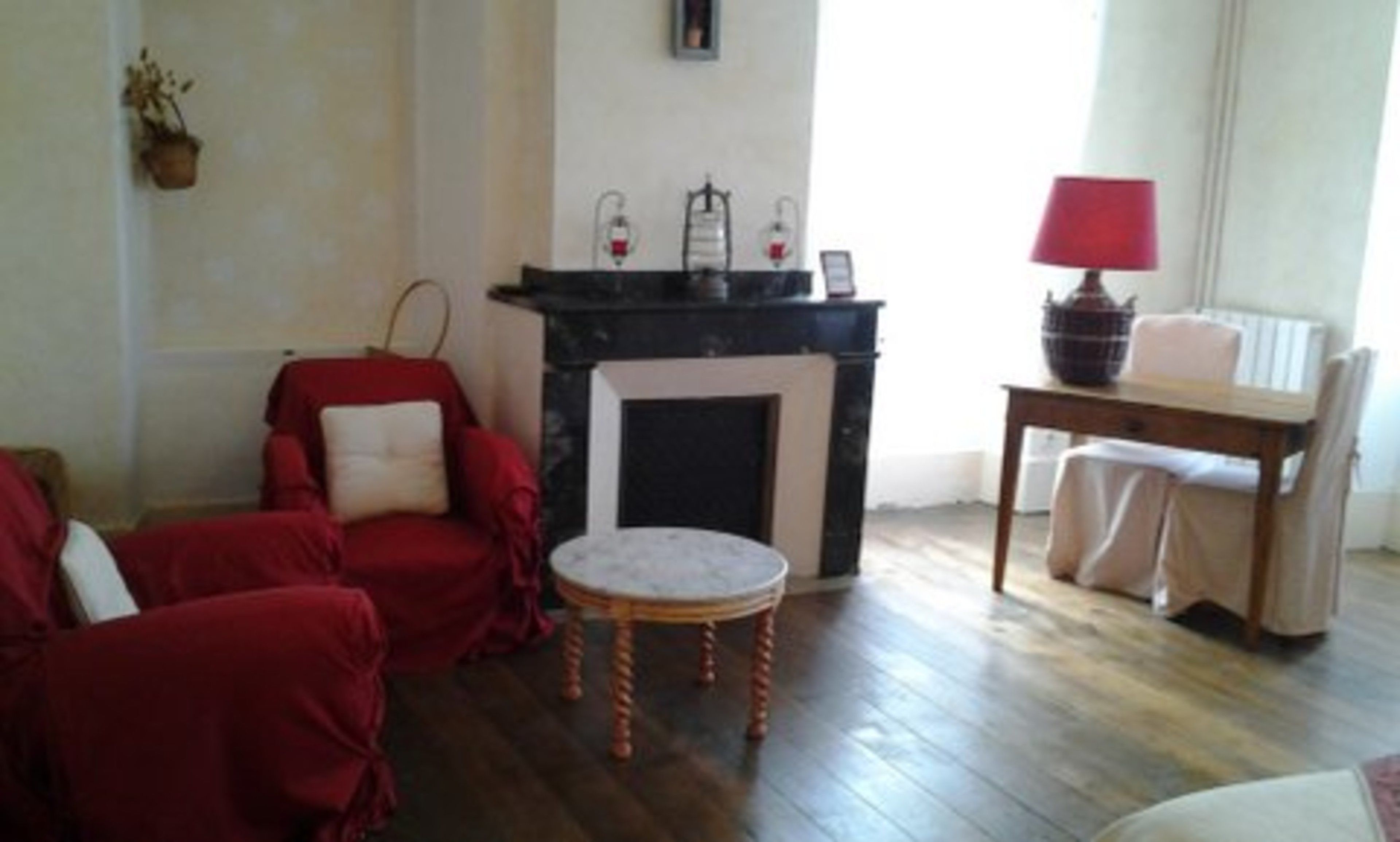 A living room with a fireplace, a red armchair, a small round table, and a lamp.