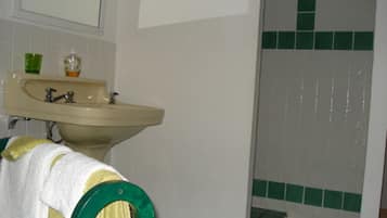 A bathroom with a sink, mirror, green-tiled shower, and a towel hanging on a green towel rack.