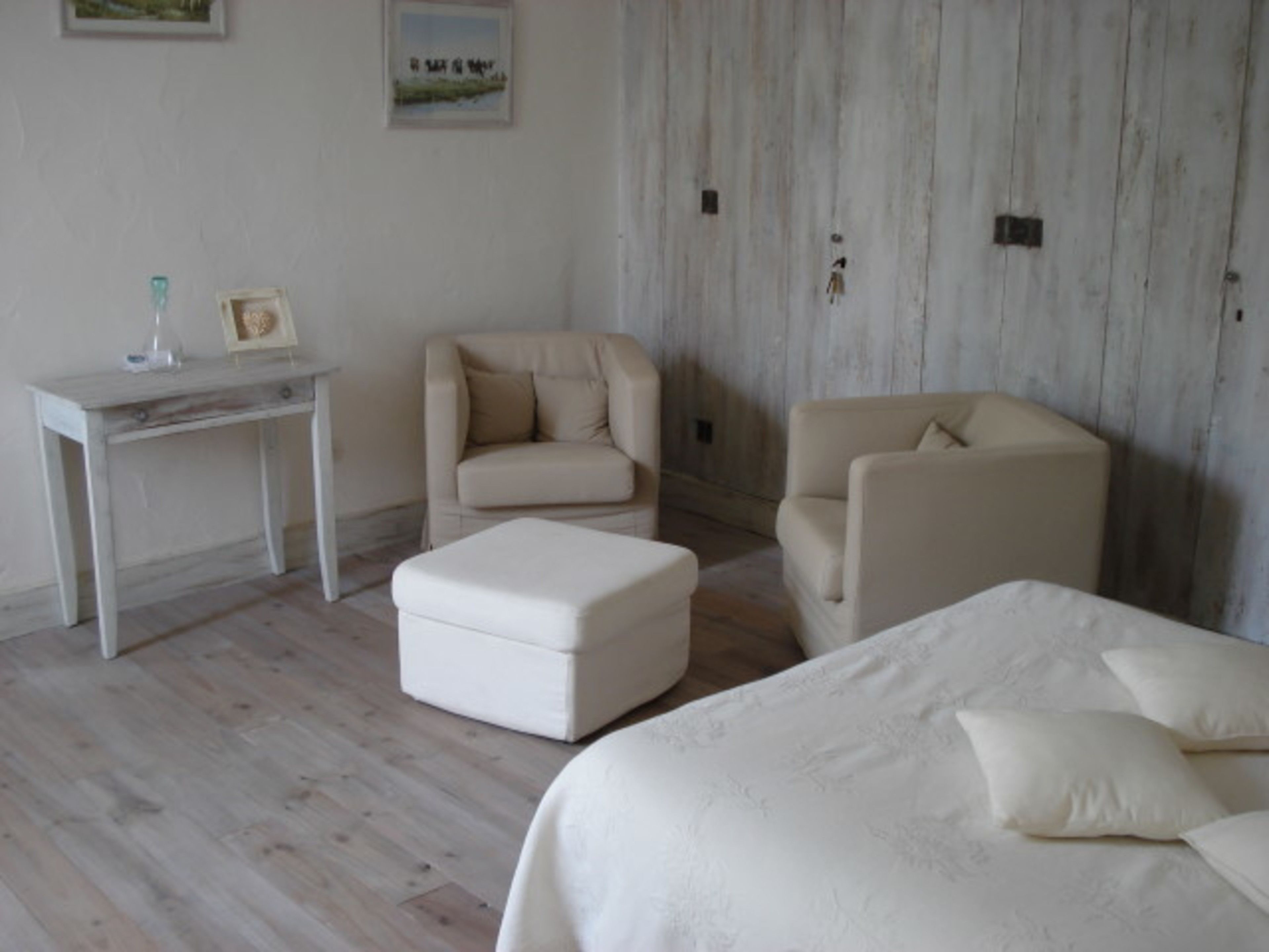 A bedroom with a bed, two armchairs, a small table, and a wall with a picture.