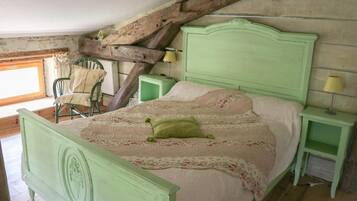 A green-painted bed with a floral bedspread and a single green pillow in a rustic room with exposed wooden beams and a window.