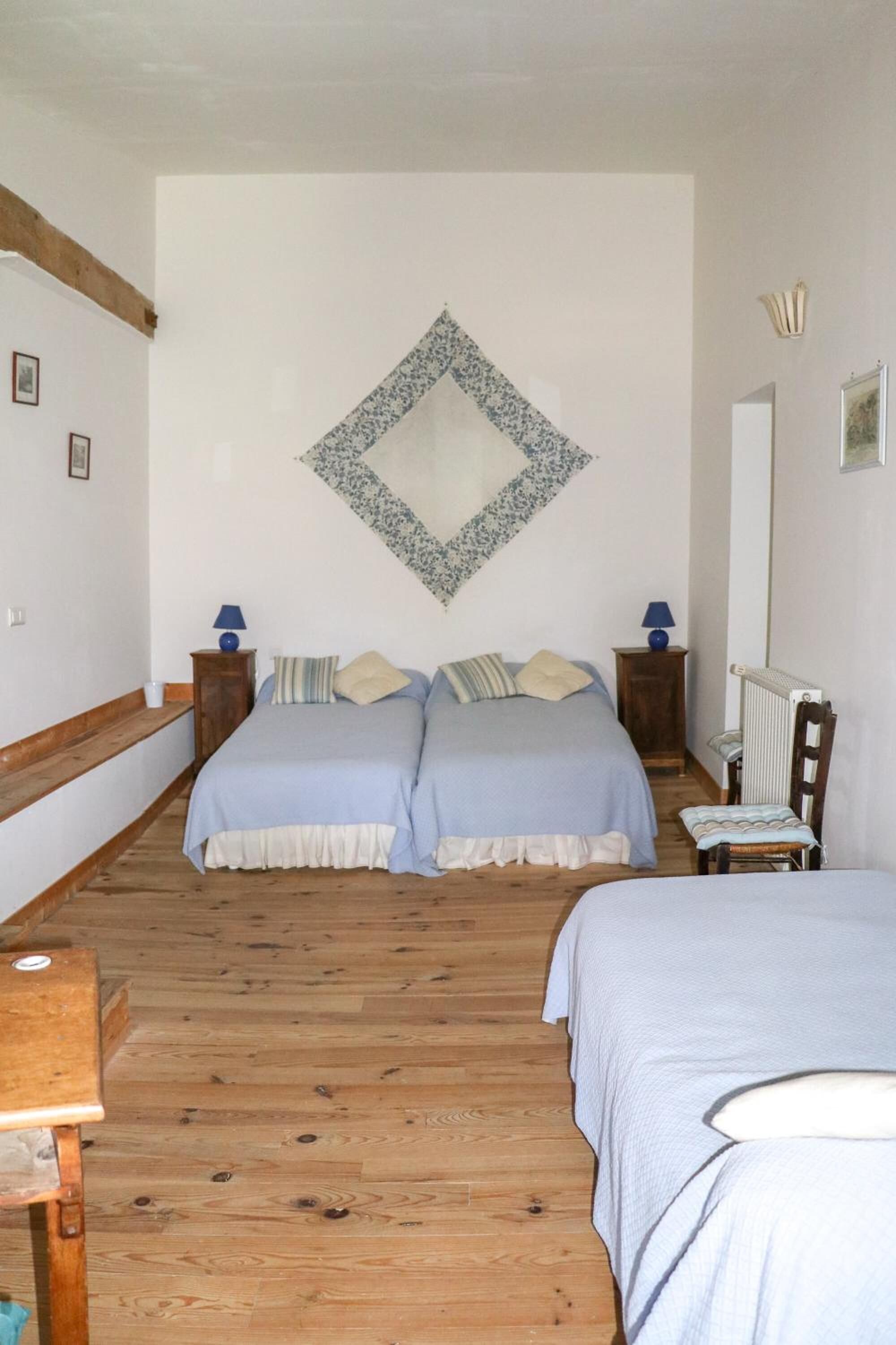 Quarto com duas camas, piso de madeira, radiador e espelho fixado na parede.