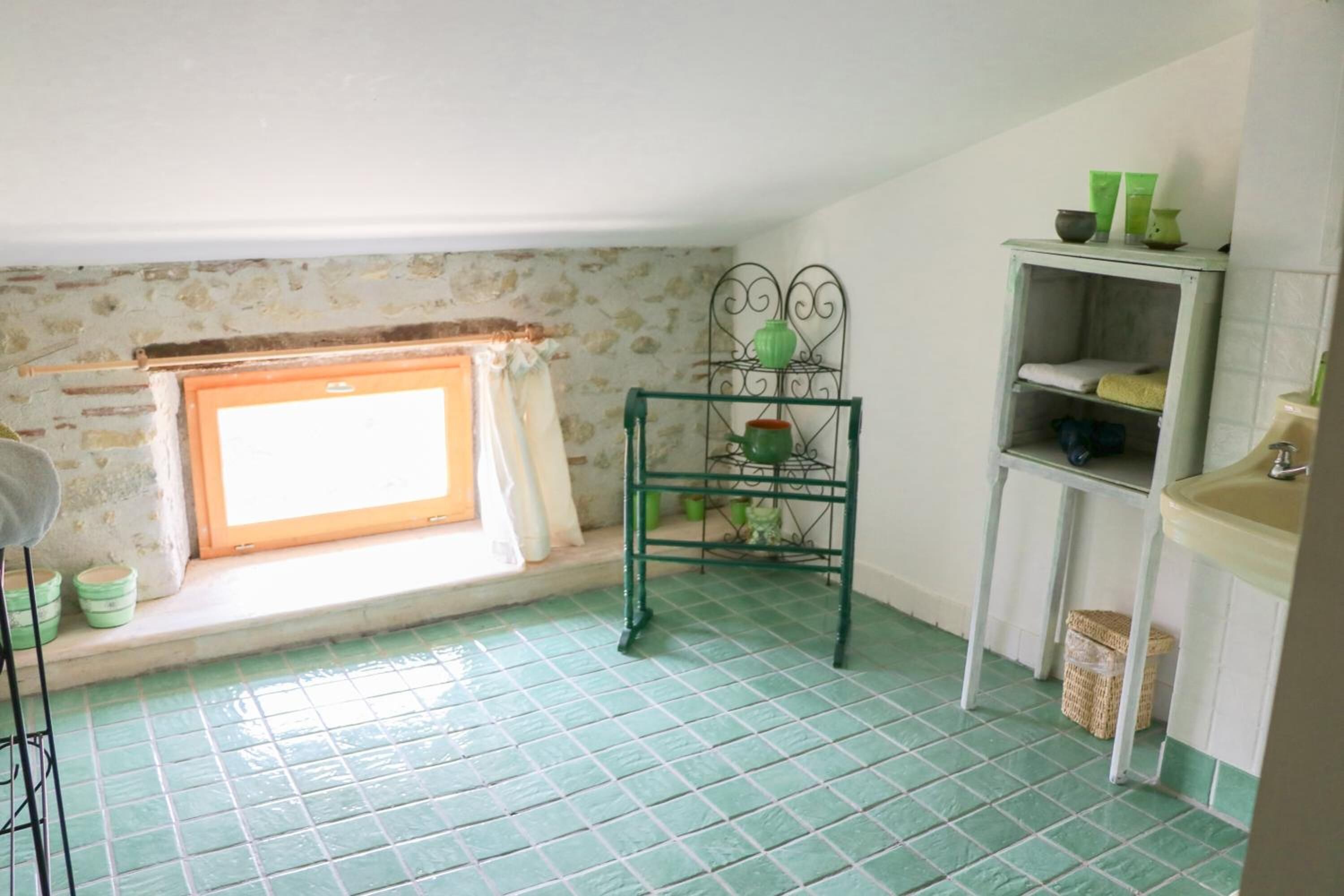 A small, tiled room with a window, a metal shelf with items, and a sink.