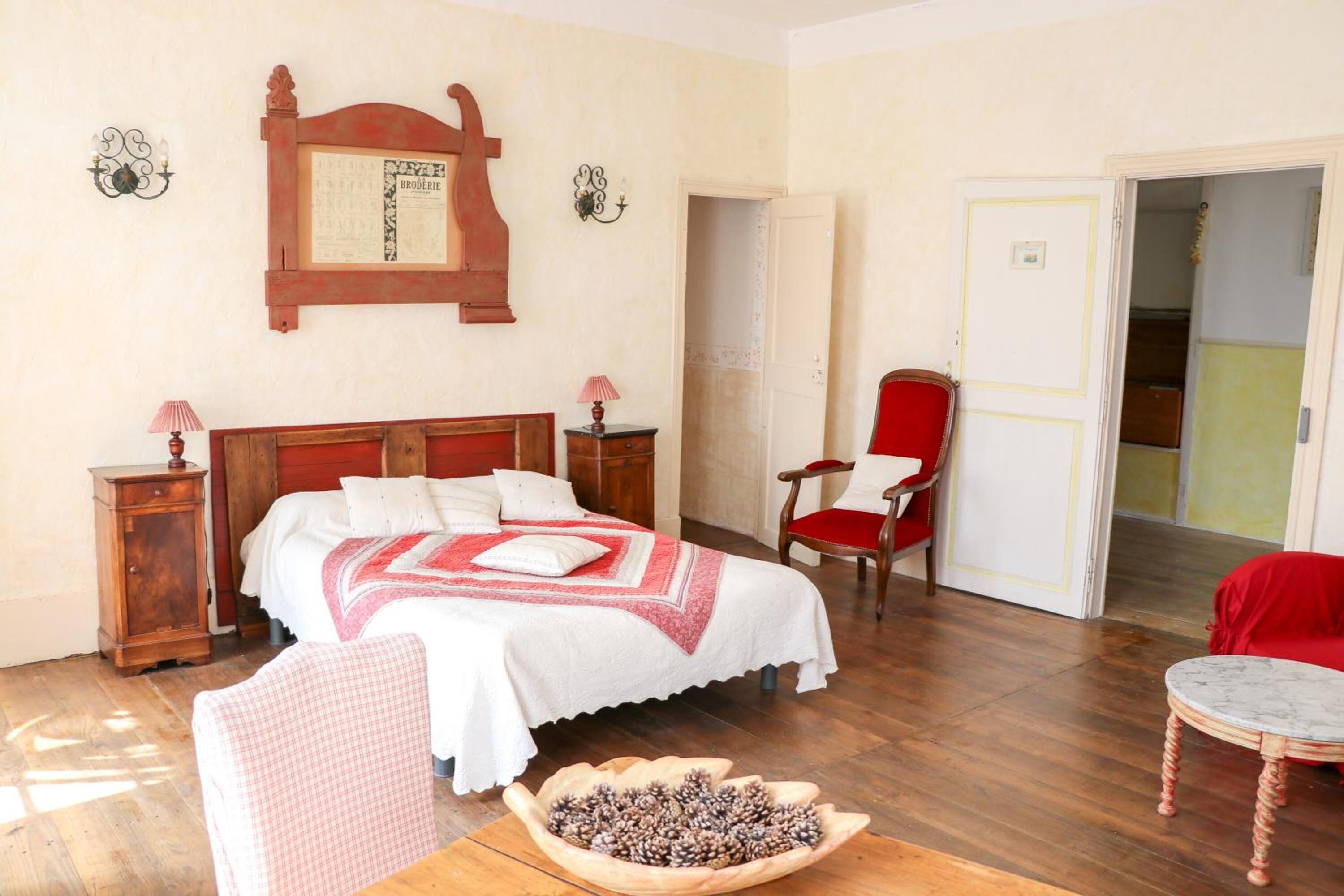 Una camera da letto con un letto in legno, una sedia rossa, un tavolino e una ciotola di legno sul pavimento.