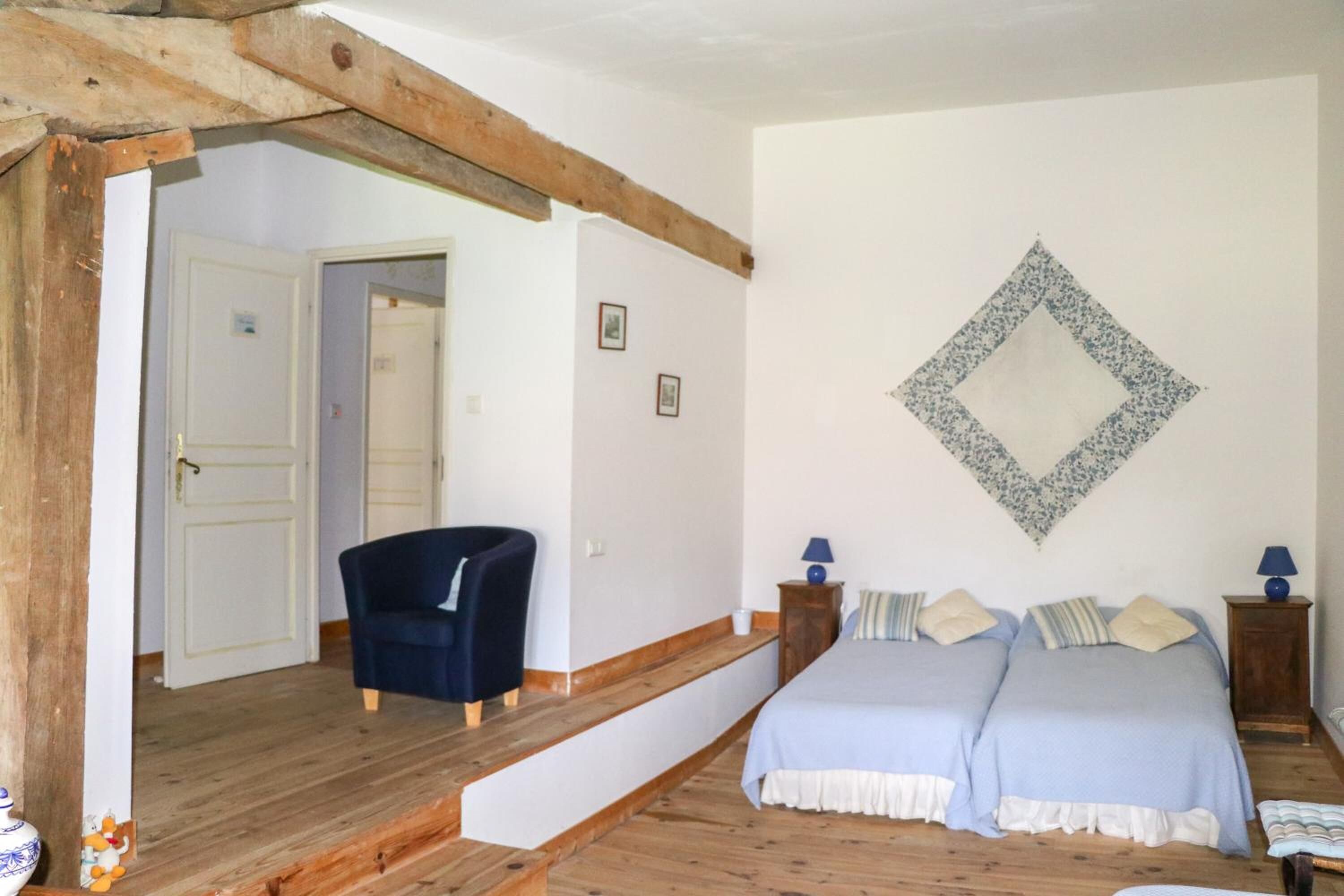 A bedroom with two beds, a chair, and a wooden staircase.