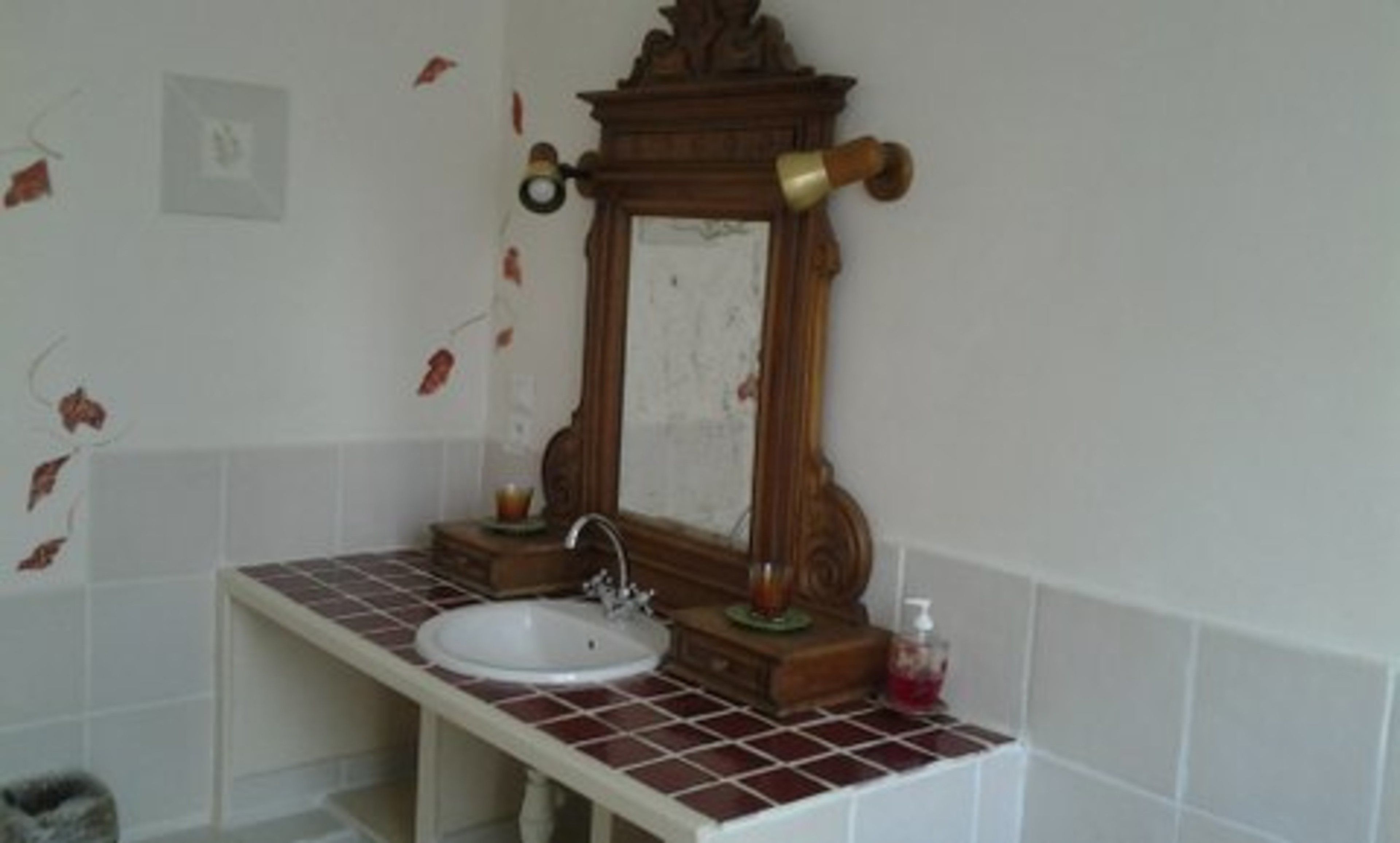 A bathroom with a white sink, a wooden-framed mirror, and a red-tiled countertop.