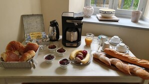 Una mesa de desayuno con cruasanes, pan, mermeladas, una cafetera y una ventana con vistas a la vegetación.