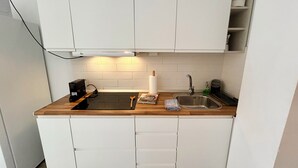 Una cocina compacta con armarios blancos, encimera de madera, lavabo integrado y cafetera.