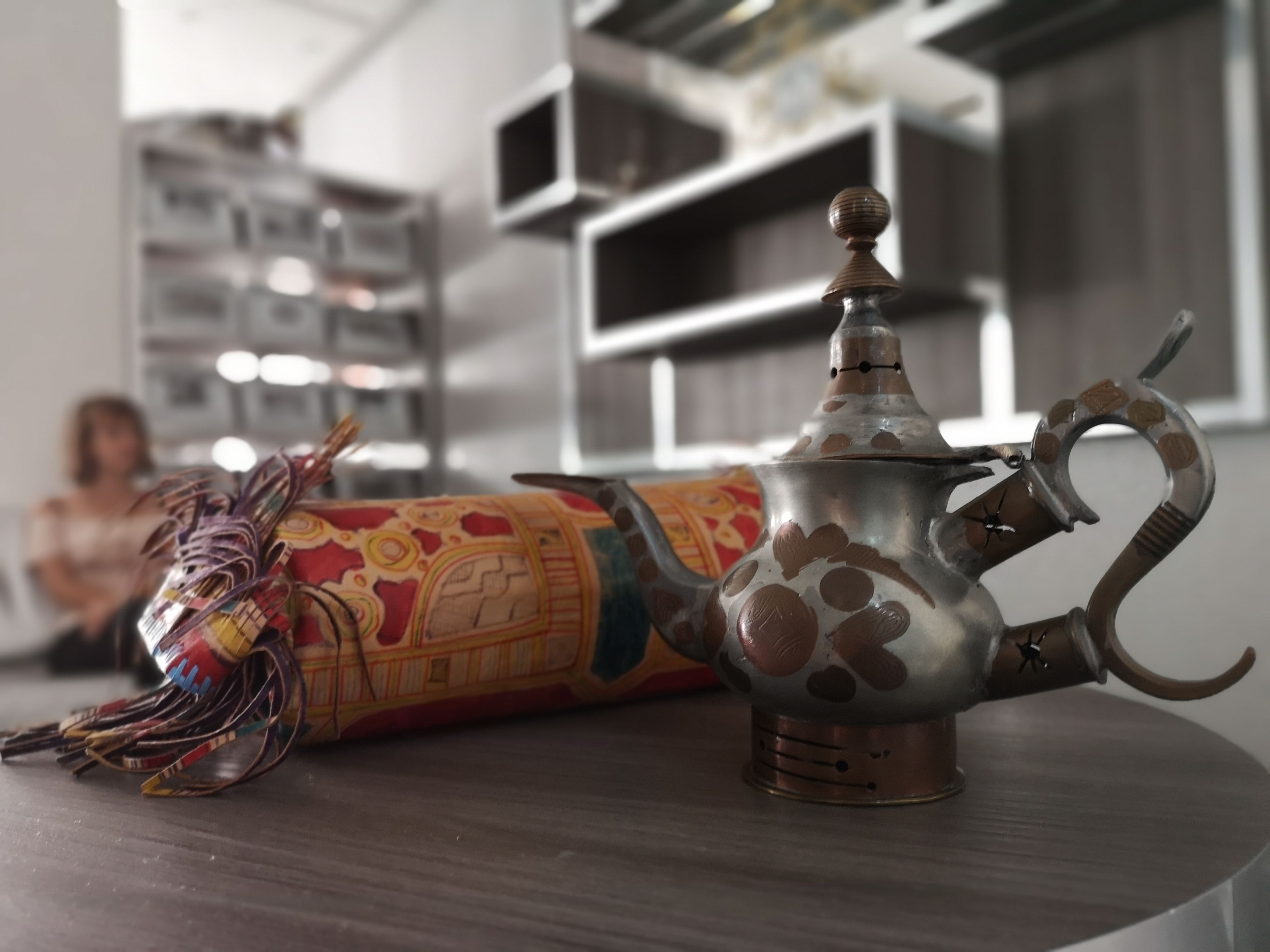 A decorative metal teapot with a handle and spout, placed on a wooden surface.
