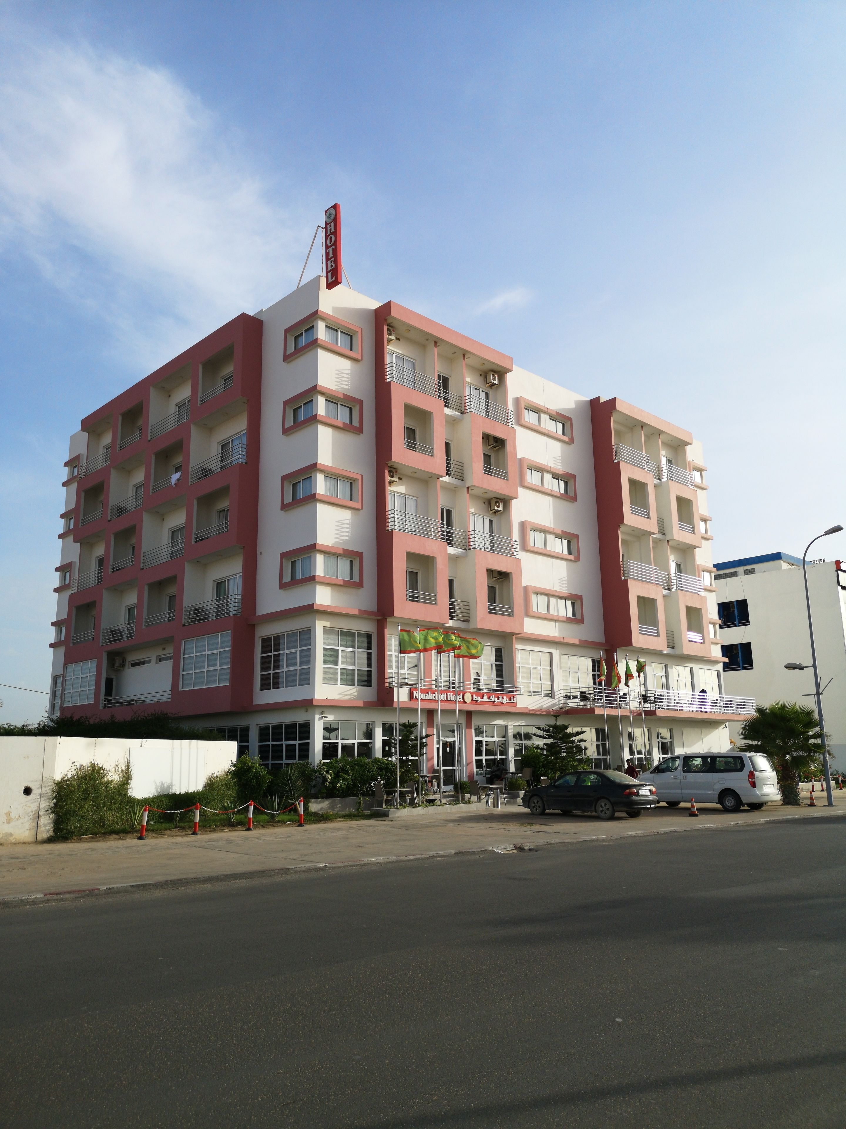 A multi-story hotel with a red and white facade, balconies, and a sign indicating it is a hotel.