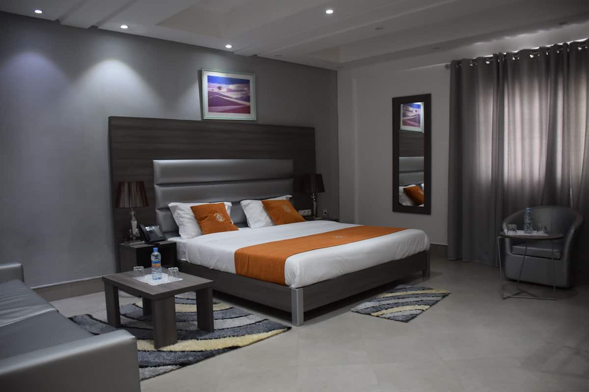 A modern hotel room with a large bed, a bedside table, a chair, and a mirror.