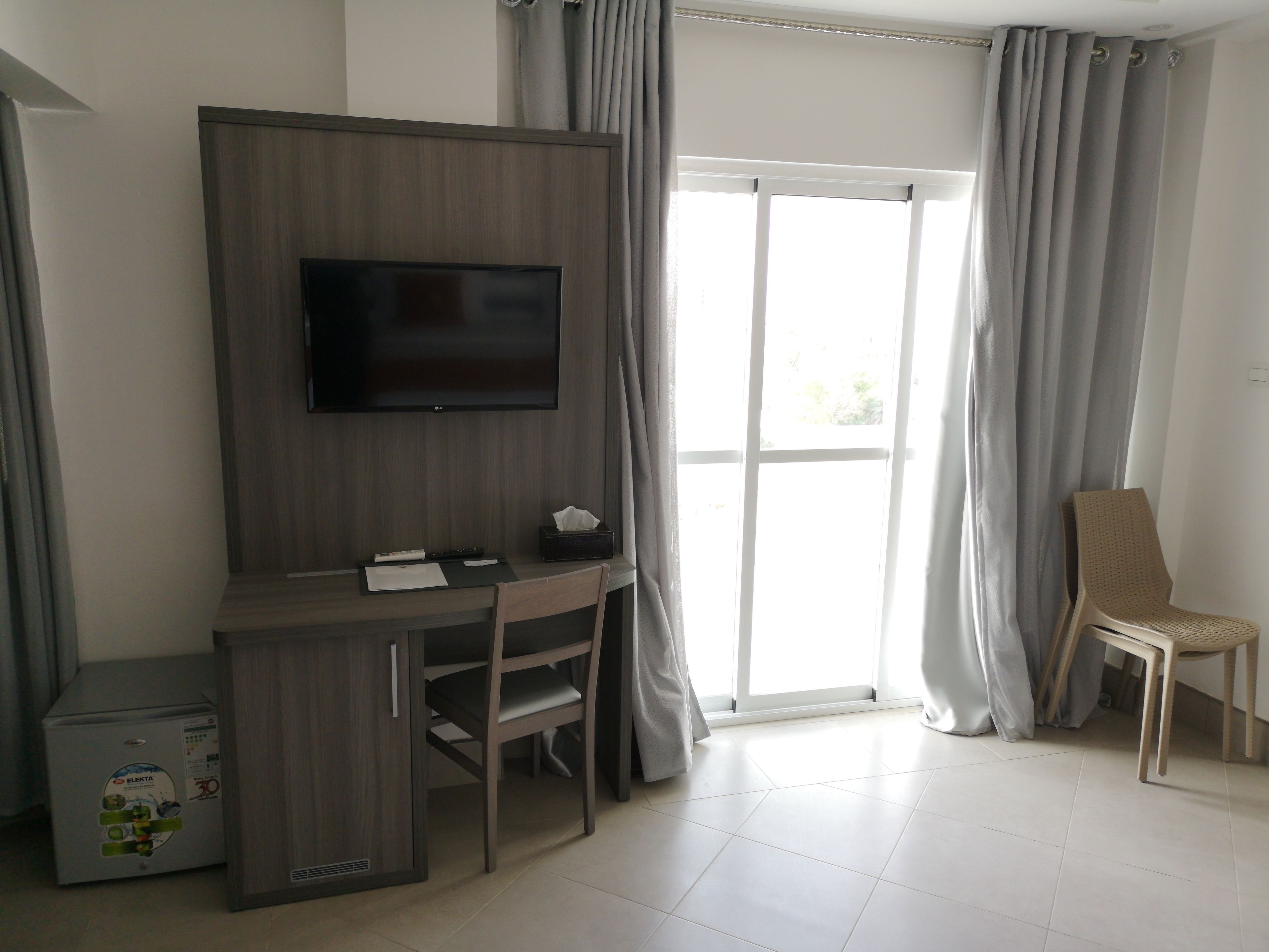 Ein Hotelzimmer mit einem Holztisch, einem Fernseher, einem Sessel und einem Fenster mit Vorhängen.