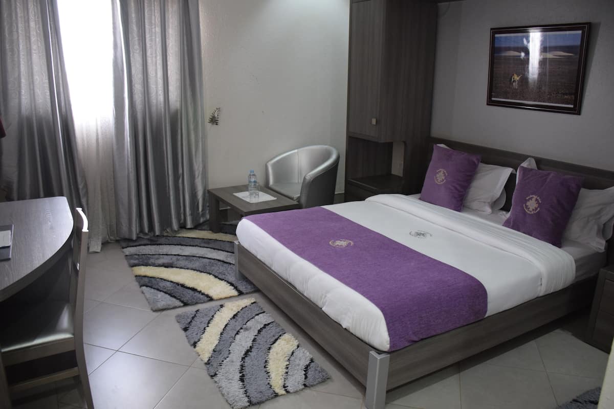 A hotel room with a bed, a chair, a desk, and a nightstand.