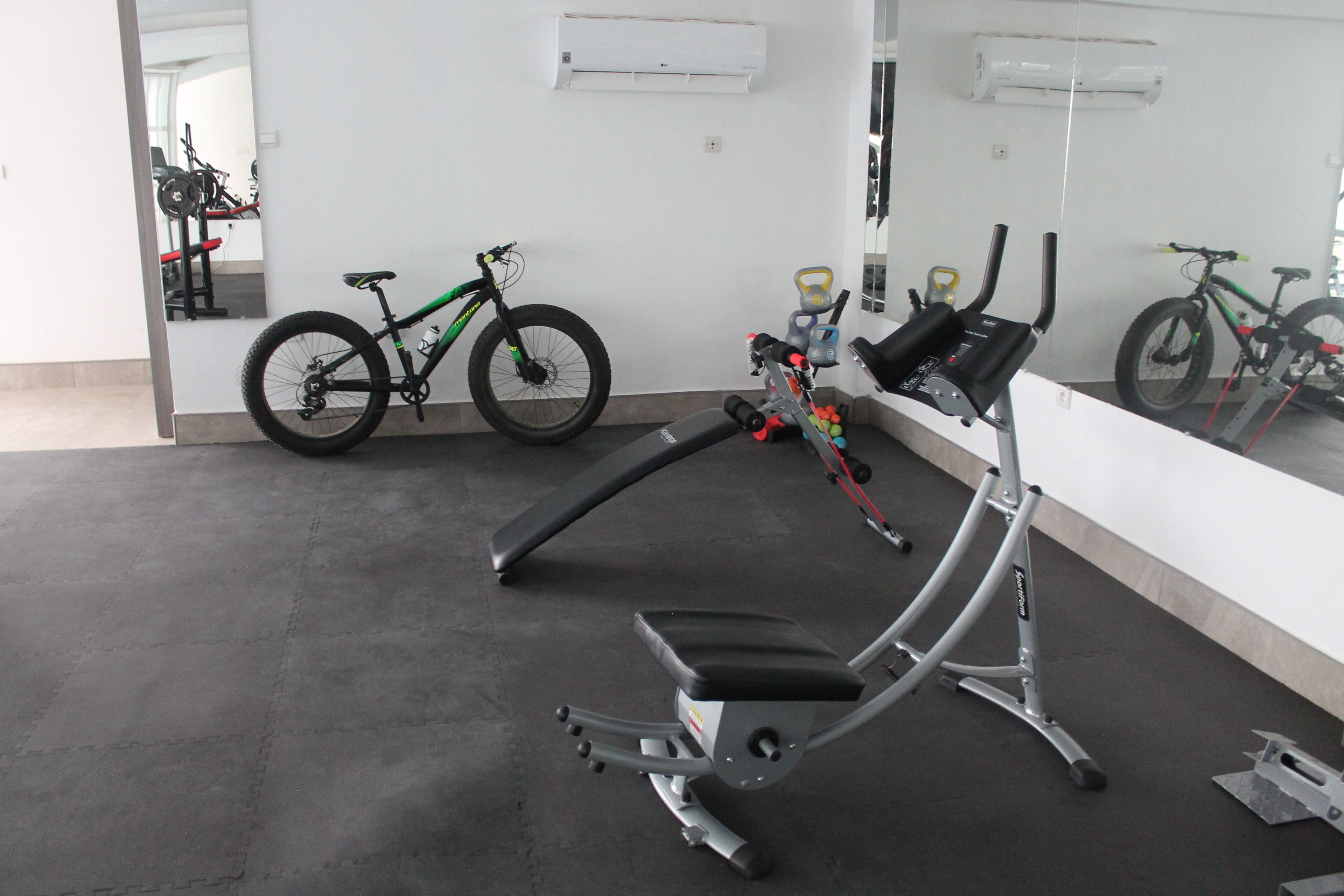 A gym with exercise equipment, a stationary bike, and a mirror reflecting the room.
