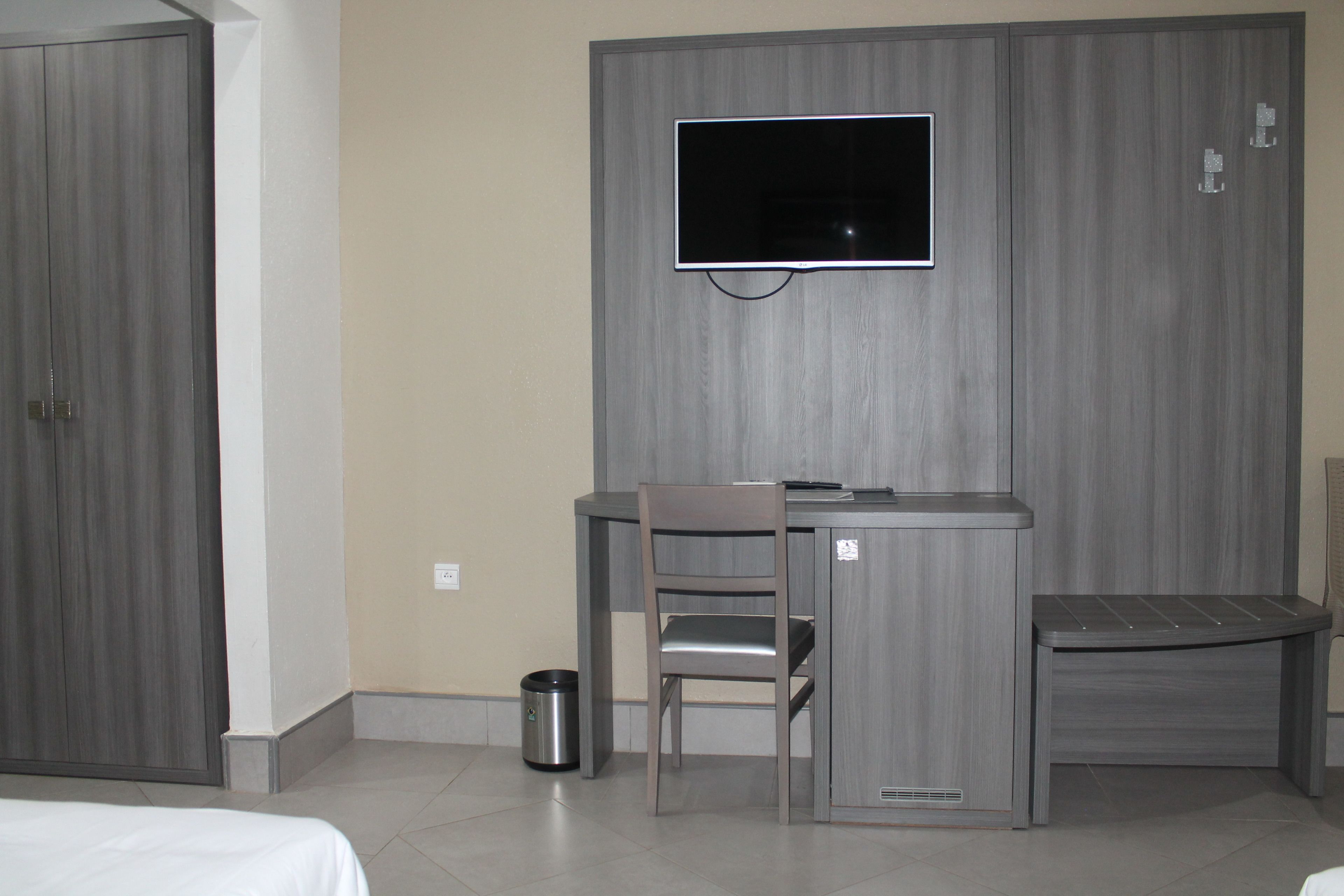 Una habitación de hotel con una cama, un escritorio con silla, un televisor montado en la pared y un cesto de basura.