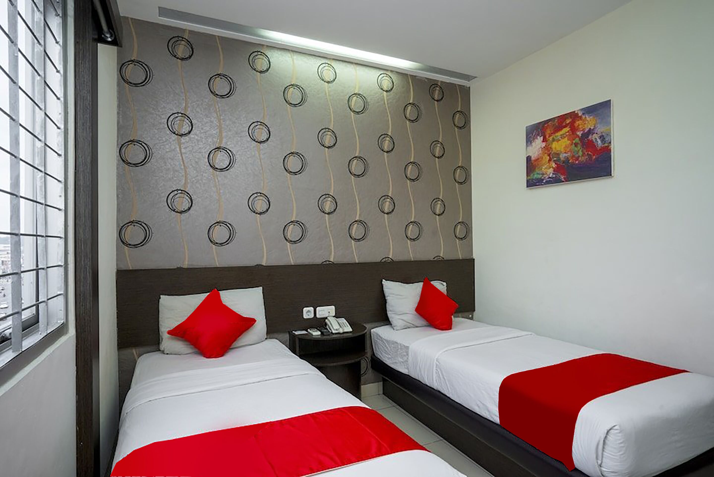 Quarto de hotel com duas camas, uma mesinha de cabeceira, um telefone e um quadro na parede.