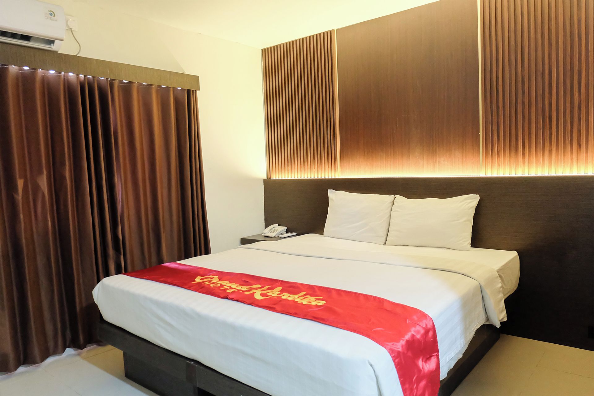 A hotel room with a bed, a nightstand, a telephone, and a curtain.