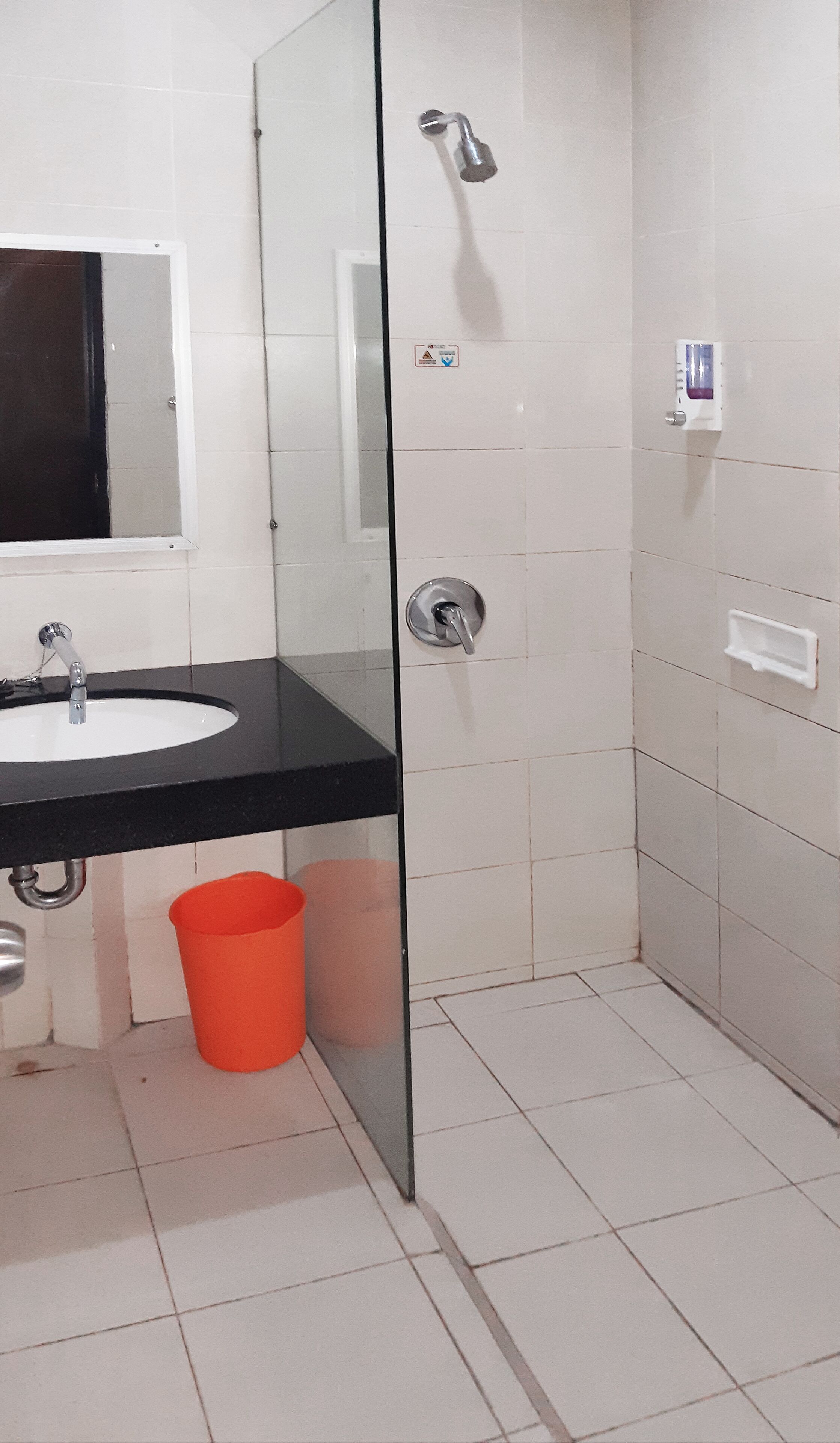 Un baño con un lavamanos blanco, un espejo, una ducha y un cubo rojo.