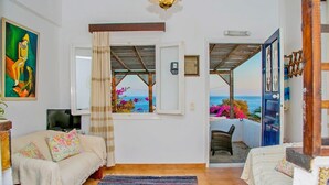 Een gezellige kamer met een bed, een televisie, een raam met uitzicht op zee en een balkon met bloemen.