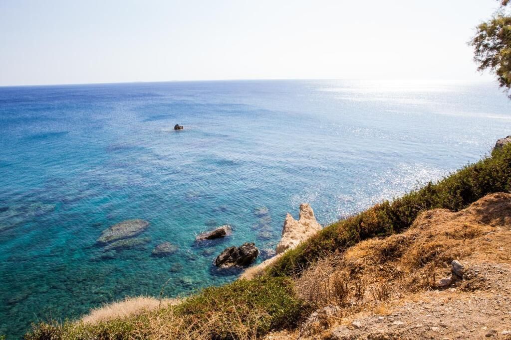 Eine Küstenlandschaft mit klarem, blauem Meer, Felsen und vereinzelter Vegetation.
