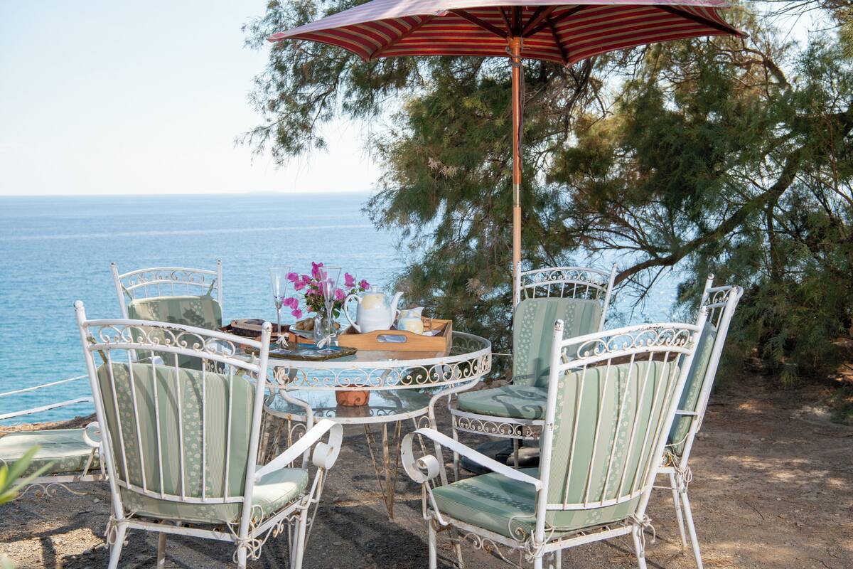 Una mesa junto a la playa con sillas y una sombrilla, con vista al mar.