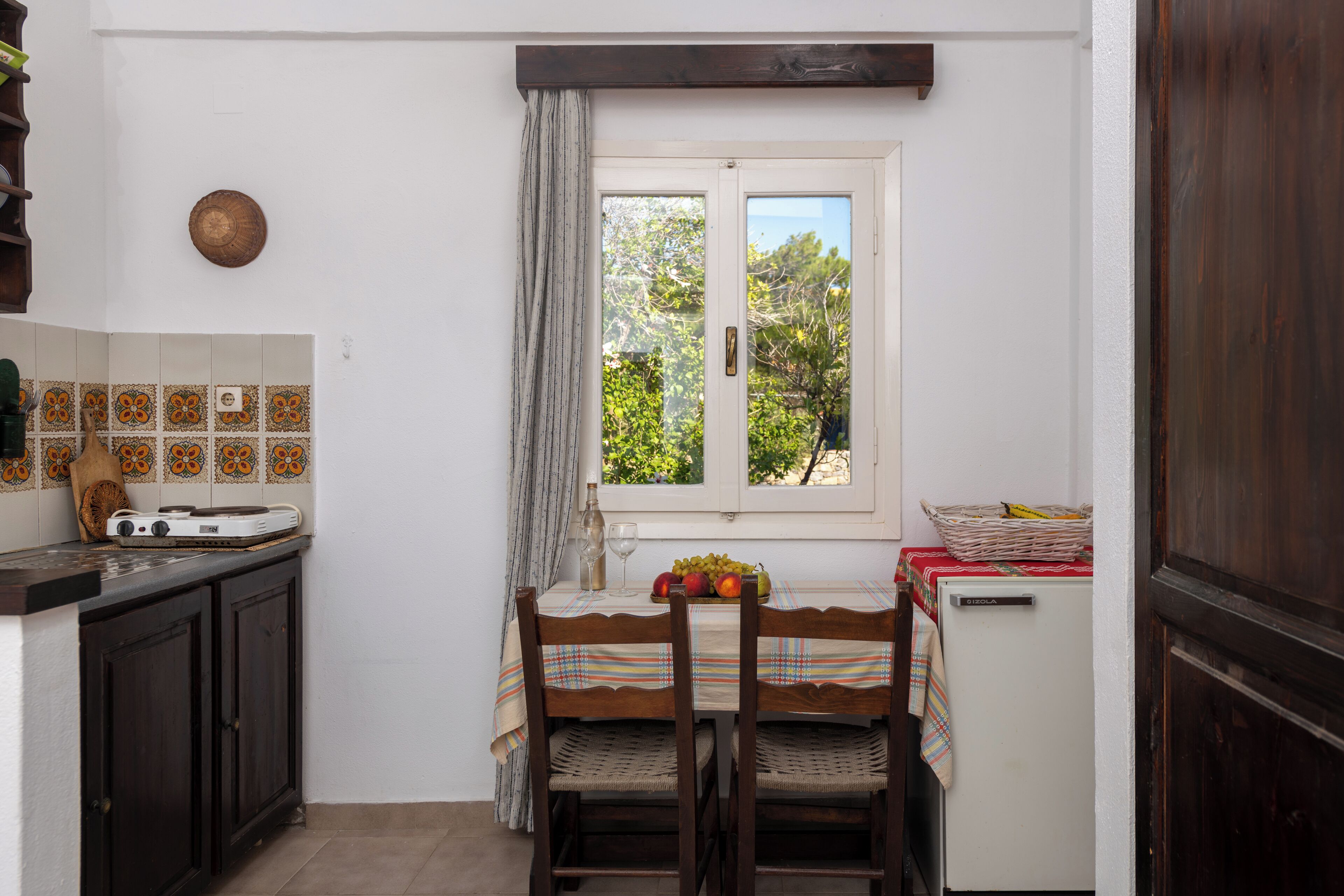 A compact kitchen with a dining table, chairs, a refrigerator, and a window with curtains.