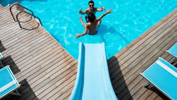 En pool med en vattenrutschkana, ett trädäck och solstolar.