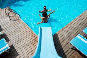 A pool with a slide, wooden deck, and lounge chairs. - Hotel Antibes (Riccione)