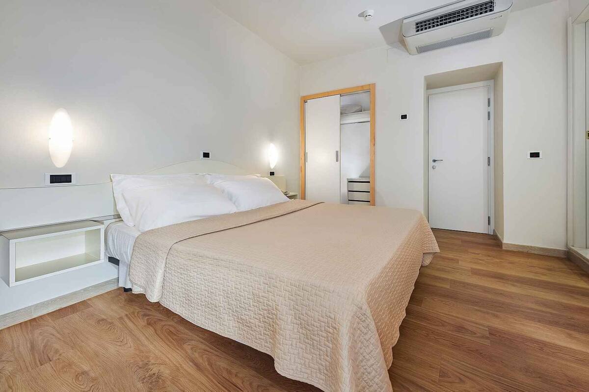 Quarto com cama, mesas de cabeceira, guarda-roupa e espelho.