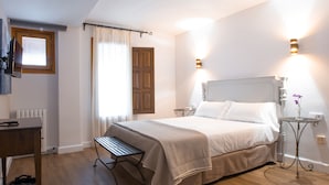 A bedroom with a bed, bedside tables, a bench, a small table with a vase, and a window with curtains. - Hotel Jaime I (Mora de Rubielos)