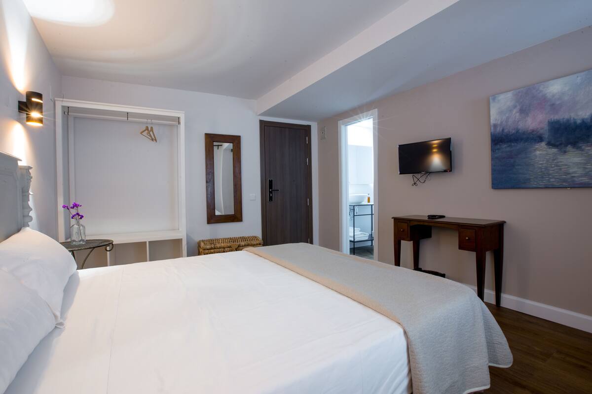 A hotel room with a large bed, a desk, a television, and a painting on the wall.