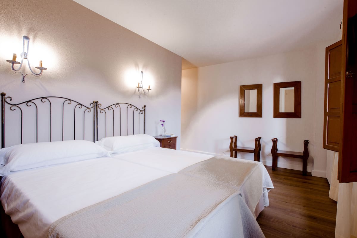 A hotel room with a double bed, a nightstand, a mirror, and a wooden floor.