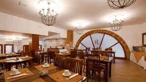 A dining area with multiple tables and chairs, chandeliers, and a large arched window. - Hotel Jaime I (Mora de Rubielos)