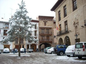 Une rue enneigée, bordée de voitures garées, et un immeuble doté de balcons et d’une arche.