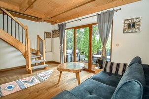Amplia sala de estar con una escalera de madera, una mesa de centro redonda de madera, un sofá azul oscuro y vistas al exterior a través de grandes puertas corredizas de vidrio.